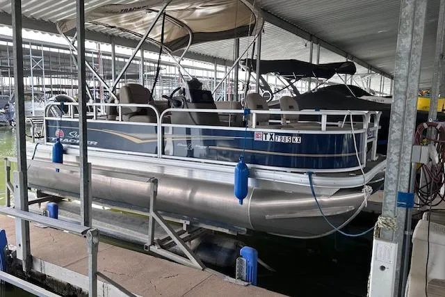The Image of 2024 Sun Tracker Bass Buggy 18 DLX pontoon boat docked in a covered marina. - 0