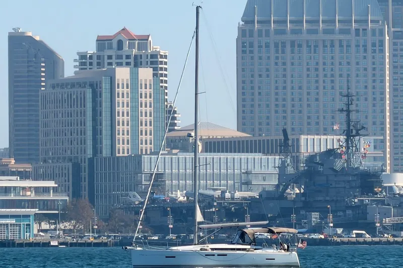 Slide: The Image of 2015 Jeanneau Sun Odyssey 409 sailing near urban skyline and naval ship. - 2
