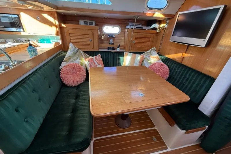 Slide: The Image of Cozy dining area in a 2004 Catalina 36 MkII sailboat with green cushions and wooden table. - 2