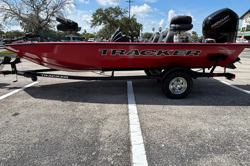 The Image of 2026 Tracker Pro Team 175 boat in a parking lot, featuring a red hull and Mercury engine. - 0