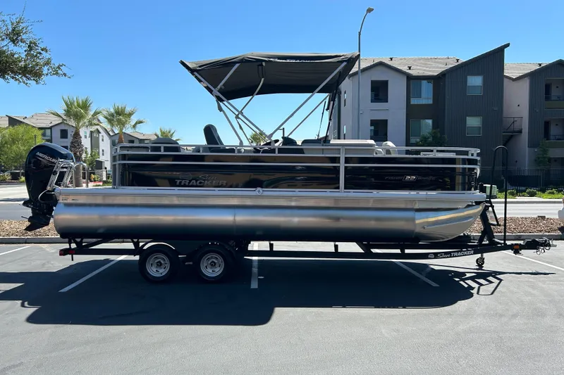 The Image of 2026 Sun Tracker Fishin' Barge 22 DLX pontoon boat on trailer in parking lot. - 0