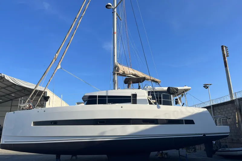 Slide: The Image of Catamaran Bali 4.1 sailing on calm sea, 2019 model, with distant boat and rocky shoreline. - 4