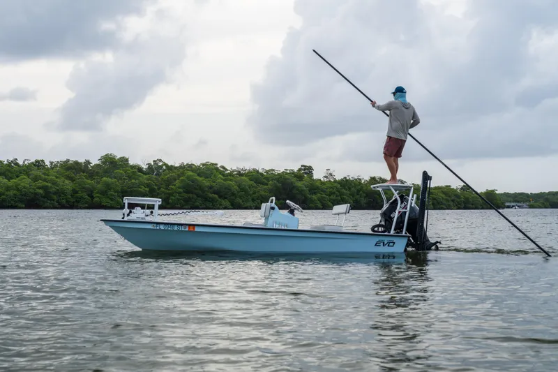 The Image of 2020 East Cape 18 EVO boat on water, person poling, cloudy sky, lush greenery background. - 0