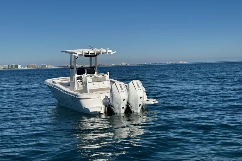 Slide: The Image of 2026 Caymas 291 boat with dual engines on open water, city skyline in background. - 2