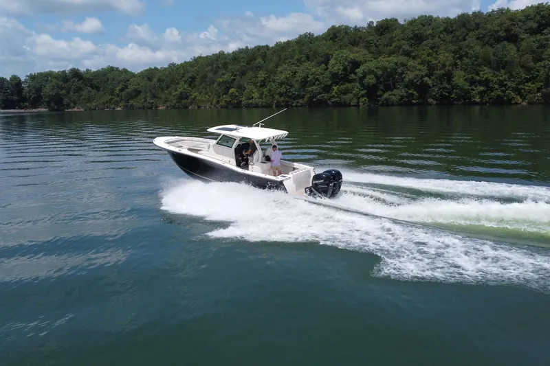 Slide: The Image of 2021 Scout 330 LXF boat cruising on a serene lake with lush green shoreline. - 17