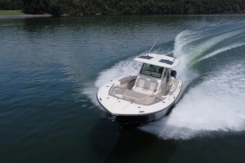 Slide: The Image of 2021 Scout 330 LXF boat cruising on a serene lake with lush green shoreline. - 3