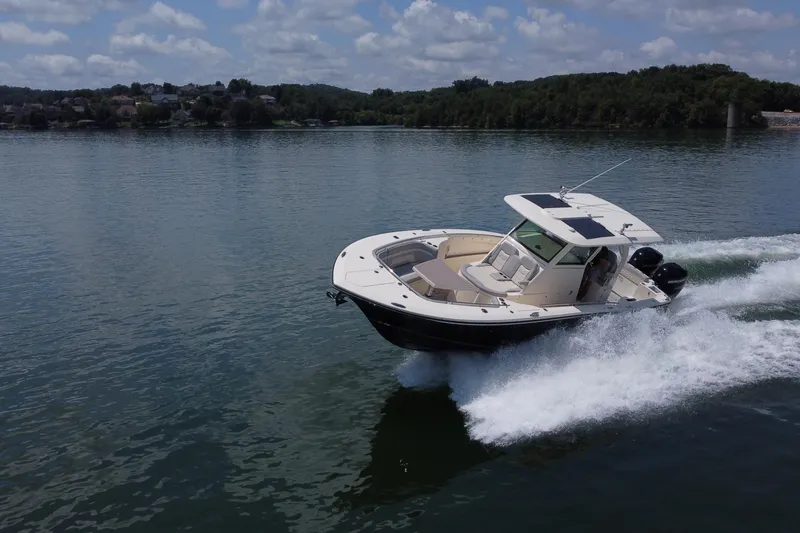Slide: The Image of 2021 Scout 330 LXF boat cruising on a serene lake under a partly cloudy sky. - 4