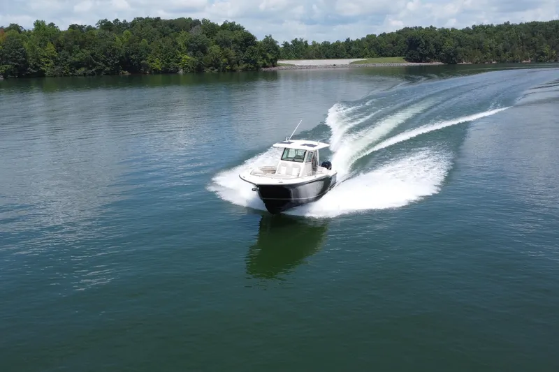 Slide: The Image of 2021 Scout 330 LXF boat cruising on a serene lake with lush green surroundings. - 9