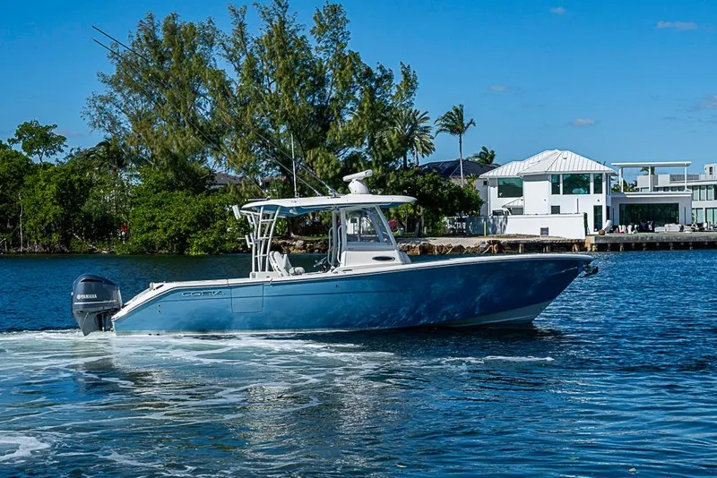 Slide: The Image of 2021 Cobia 320 Center Console boat cruising on a sunny day near waterfront homes. - 31