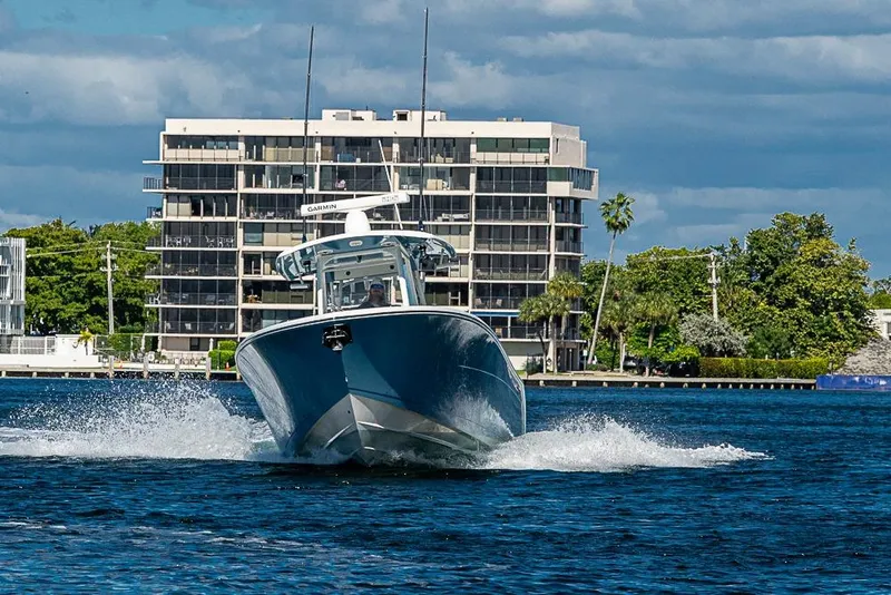 Slide: The Image of 2021 Cobia 320 Center Console boat cruising on water near modern buildings. - 41