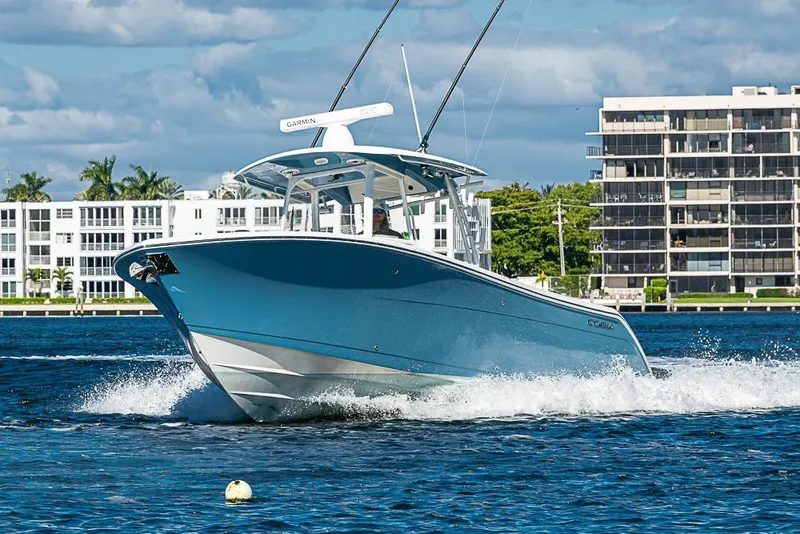 Slide: The Image of 2021 Cobia 320 Center Console boat cruising on water near waterfront buildings. - 43