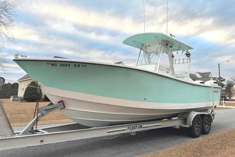 The Image of 2003 Regulator 26 Forward Seating boat on trailer, light blue hull, parked in residential area. - 0
