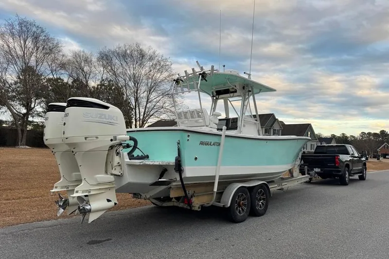 Slide: The Image of 2003 Regulator 26 Forward Seating boat on trailer, towed by a truck, under cloudy sky. - 2