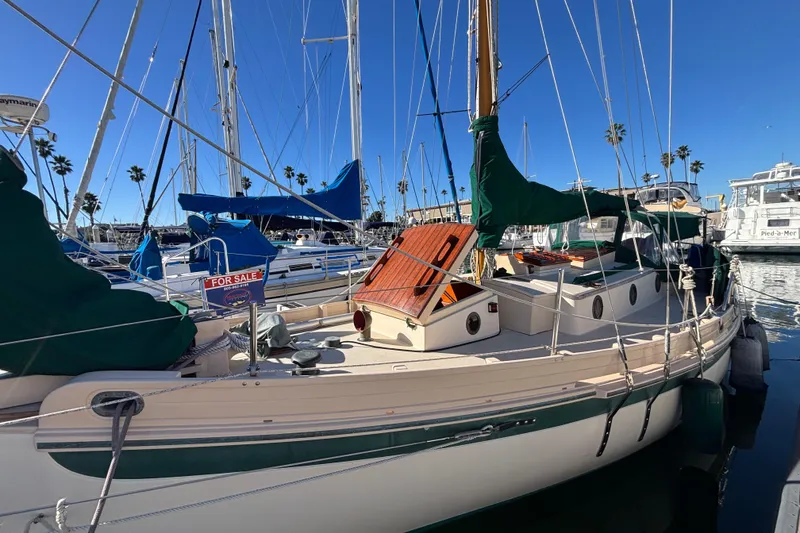 The Image of 1983 Bristol Channel Cutter 28 sailboat docked, with "For Sale" sign, in a sunny marina. - 0