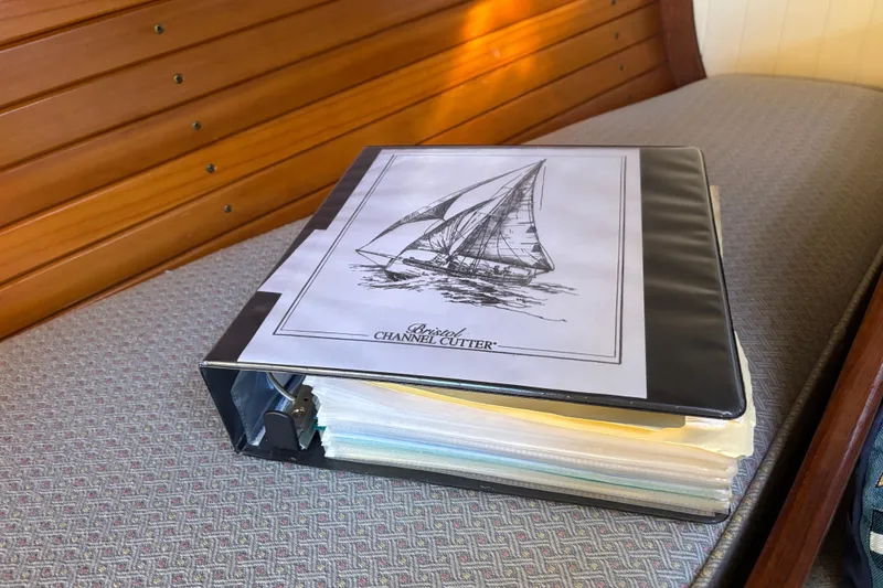 Slide: The Image of Binder with Bristol Channel Cutter 28 sailboat documents, 1983, on a wooden bench. - 50