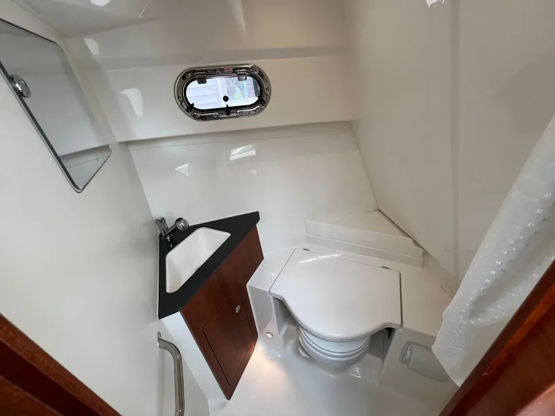 Slide: The Image of 2025 Pursuit OS 325 Offshore boat bathroom with sink, toilet, and porthole window. - 19