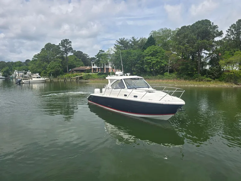 Slide: The Image of 2025 Pursuit OS 325 Offshore boat cruising on a calm river with lush greenery. - 2