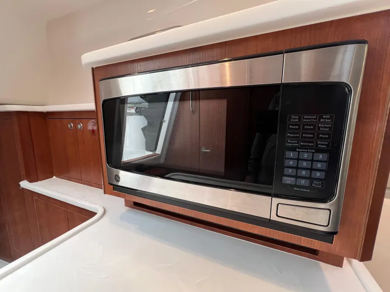 Slide: The Image of Microwave in 2025 Pursuit OS 325 Offshore boat kitchen, featuring sleek wood cabinetry. - 26