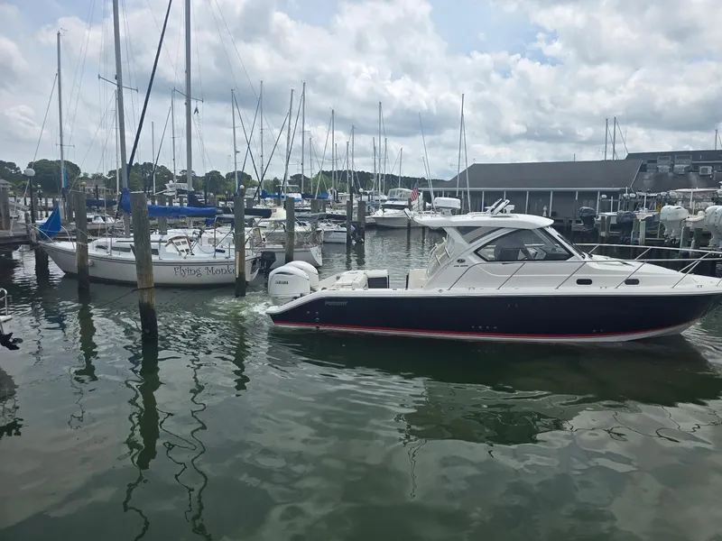 Slide: The Image of 2025 Pursuit OS 325 Offshore boat docked in a marina with sailboats and cloudy sky. - 5