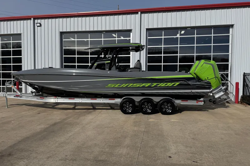 The Image of 2026 Sunsation 32 CCX boat with green accents on a trailer outside a garage. - 1
