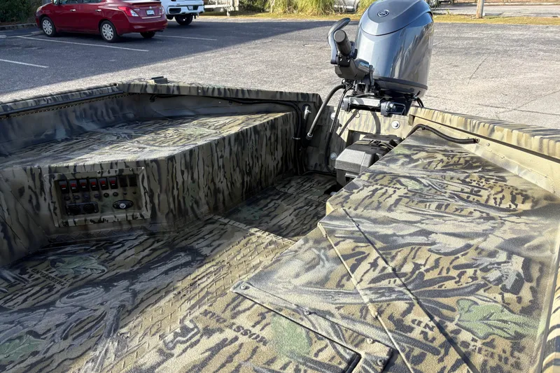 Slide: The Image of 2026 SeaArk 1752 Slayer X boat with camouflage design and outboard motor in parking lot. - 9