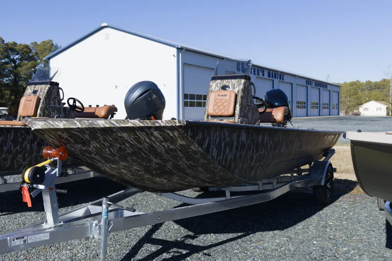 The Image of 2026 Avid 20 Rogue CC boat on trailer, camo design, parked outside marine shop. - 0
