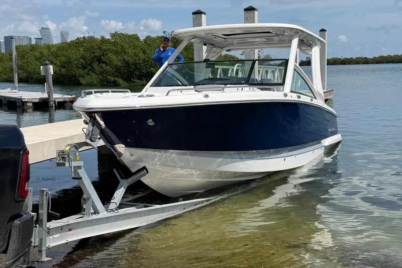 Slide: The Image of 2020 Chaparral 300 OSX boat being launched from a trailer at a scenic dock. - 10