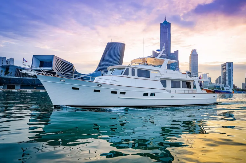 Slide: The Image of 2027 Fleming 85 Pilothouse yacht cruising near modern city skyline at sunset. - 3