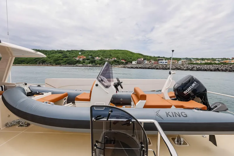 Slide: The Image of 2027 Fleming 85 Pilothouse yacht with inflatable boat and Suzuki motor, docked near scenic coastline. - 69