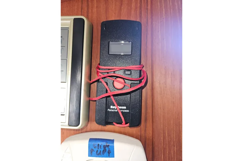 Slide: The Image of Handheld Raytheon personal compass with red cord on wooden surface, Pacific Seacraft Dana 24, 2003. - 26