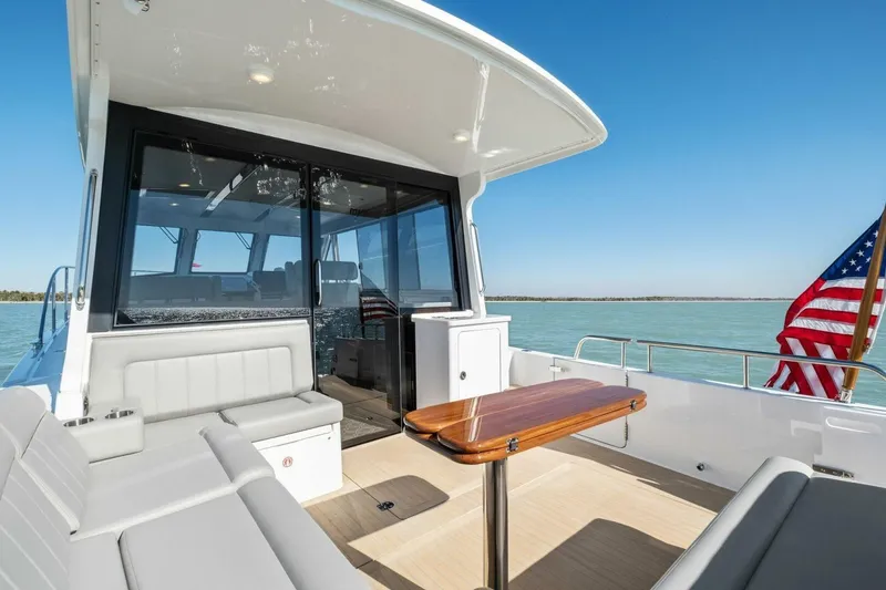 Slide: The Image of 2026 MJM 47R yacht interior with seating, table, and American flag on calm water. - 27