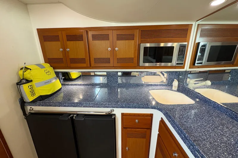 Slide: The Image of 2004 Cabo 40 Hardtop Express yacht kitchen with blue countertops, wooden cabinets, and microwave. - 22
