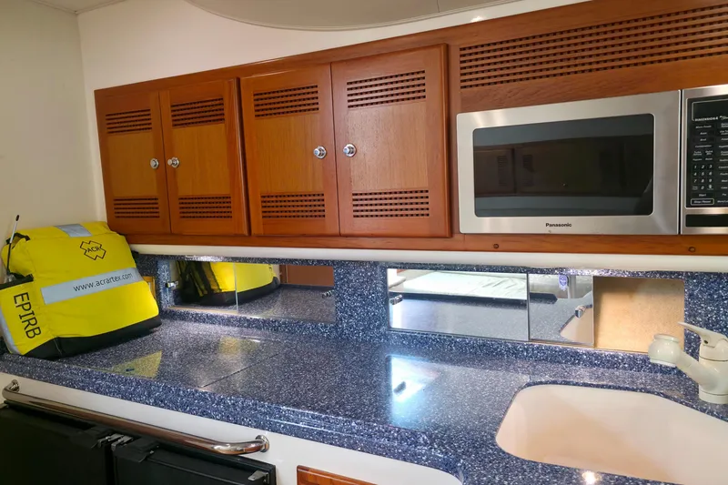 Slide: The Image of 2004 Cabo 40 Hardtop Express galley with wooden cabinets, microwave, and EPIRB safety equipment. - 27