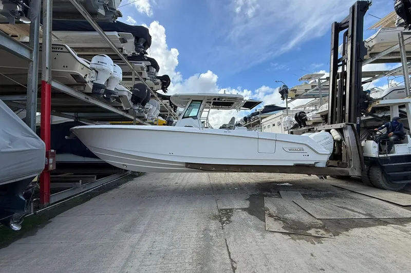 Slide: The Image of 2016 Boston Whaler 330 Outrage on forklift, surrounded by stacked boats under a blue sky. - 13