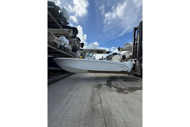 Slide: The Image of 2016 Boston Whaler 330 Outrage boat lifted by forklift under cloudy sky. - 2