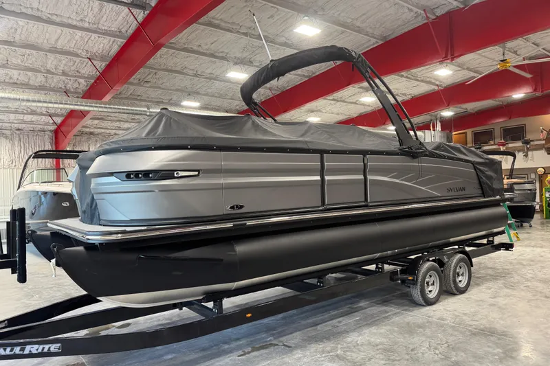 Slide: The Image of 2026 Sylvan L-5 Platinum pontoon boat in a showroom, covered and on a trailer. - 15
