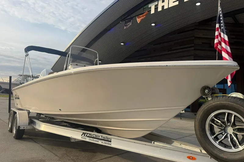 Slide: The Image of 2026 Sea Chaser 23 LX boat on trailer, parked near a building with American flag. - 7