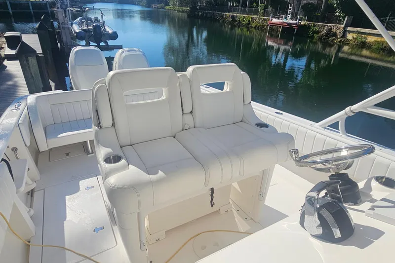 Slide: The Image of 2015 Intrepid 327 Center Console boat with white seating, docked by a serene waterway. - 9
