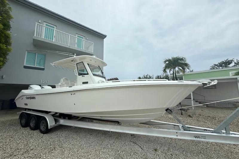 The Image of 2016 Everglades 295 Center Console boat on trailer, parked near modern building. - 0