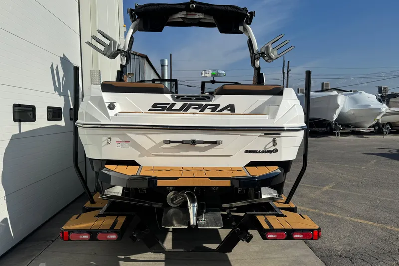 Slide: The Image of 2026 Supra SV 575 boat, rear view, parked outdoors, showcasing sleek design and swim platform. - 2