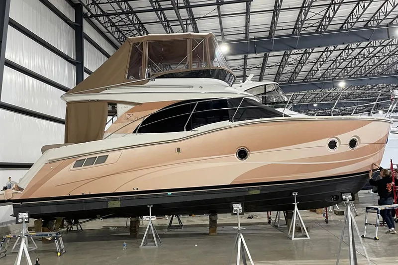 Slide: The Image of 2013 Carver C34 yacht in a warehouse, elevated on stands, with a beige and white exterior. - 49