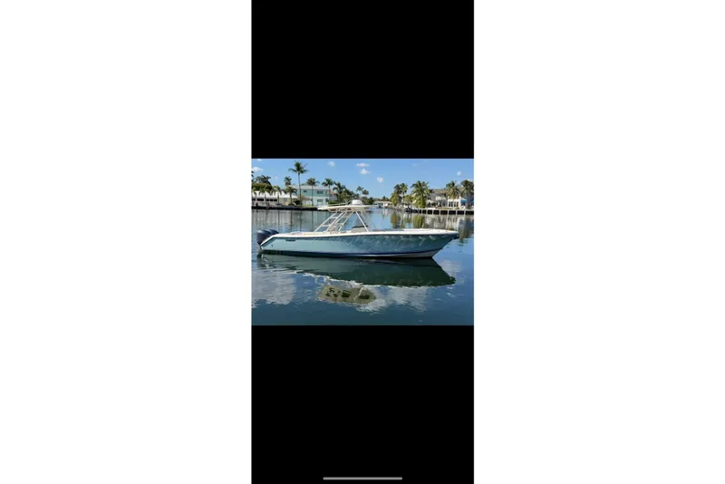 The Image of 2009 Pursuit S 310 Sport boat on calm water, surrounded by palm trees and waterfront homes. - 0