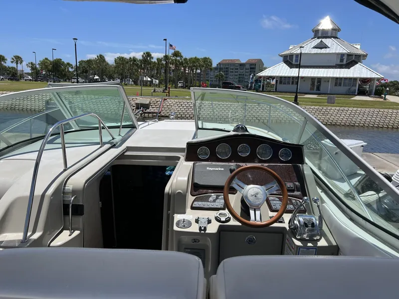Slide: The Image of 2012 Sea Ray Sundancer boat cockpit with steering wheel, docked near a waterfront building. - 23