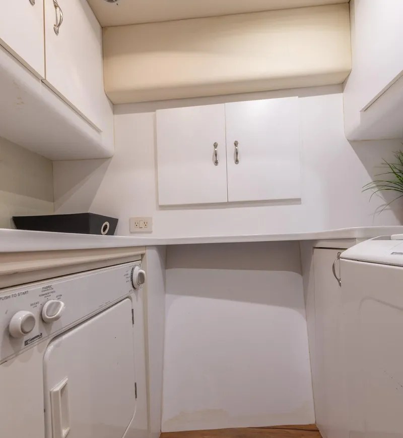 Slide: The Image of Laundry area inside 2003 Ocean Yachts 62 Super Sport EB, featuring washer, dryer, and storage cabinets. - 46