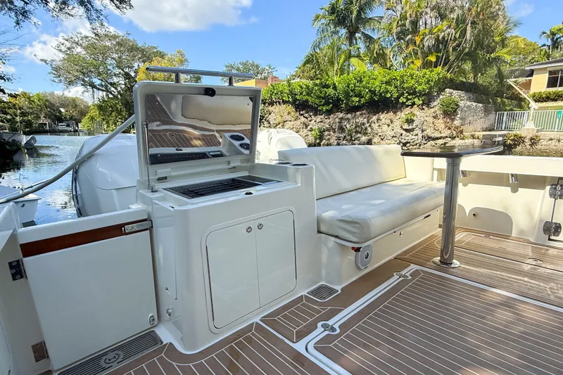 Slide: The Image of 2021 Hinckley Sport Boats 40x interior with white seating and canopy, docked by lush greenery. - 8