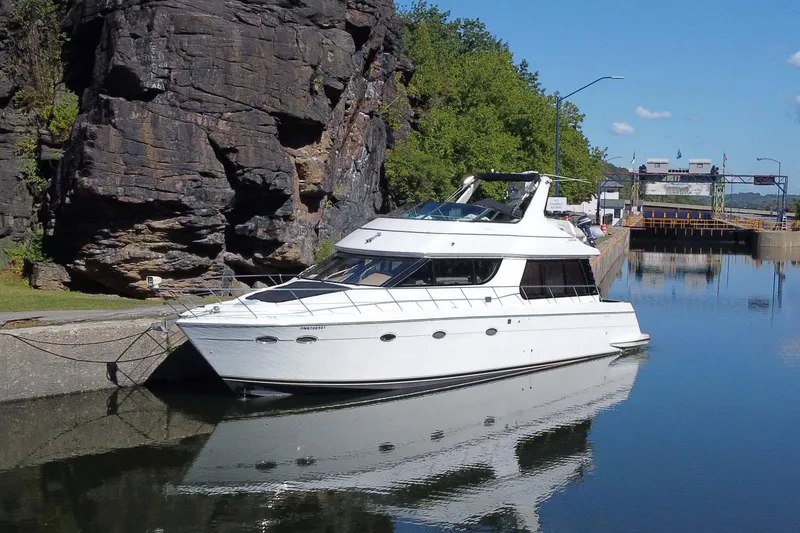The Image of 1999 Carver 530 Voyager Pilothouse yacht docked by rocky shoreline. - 1