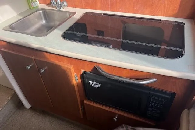 Slide: The Image of 2004 Bayliner 242 Classic boat kitchen with sink, stove, and microwave. - 18
