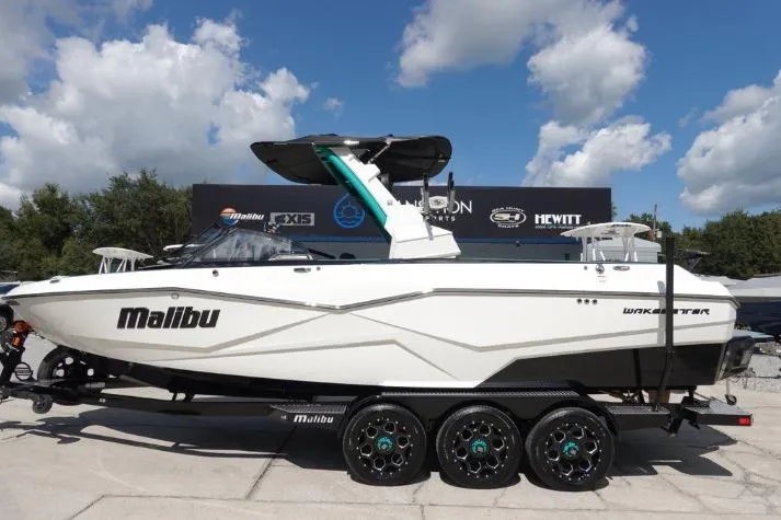 The Image of 2022 Malibu Wakesetter 25 LSV boat on trailer, displayed outdoors under a cloudy sky. - 0