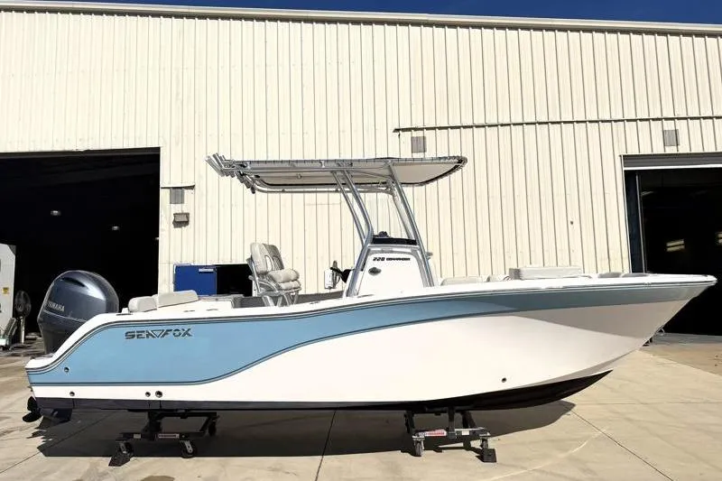 The Image of 2023 Sea Fox 228 Commander boat with blue and white hull, parked outside a warehouse. - 0