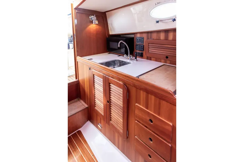 Slide: The Image of 2005 Hinckley Picnic Boat EP interior with wooden cabinetry and compact kitchen area. - 10